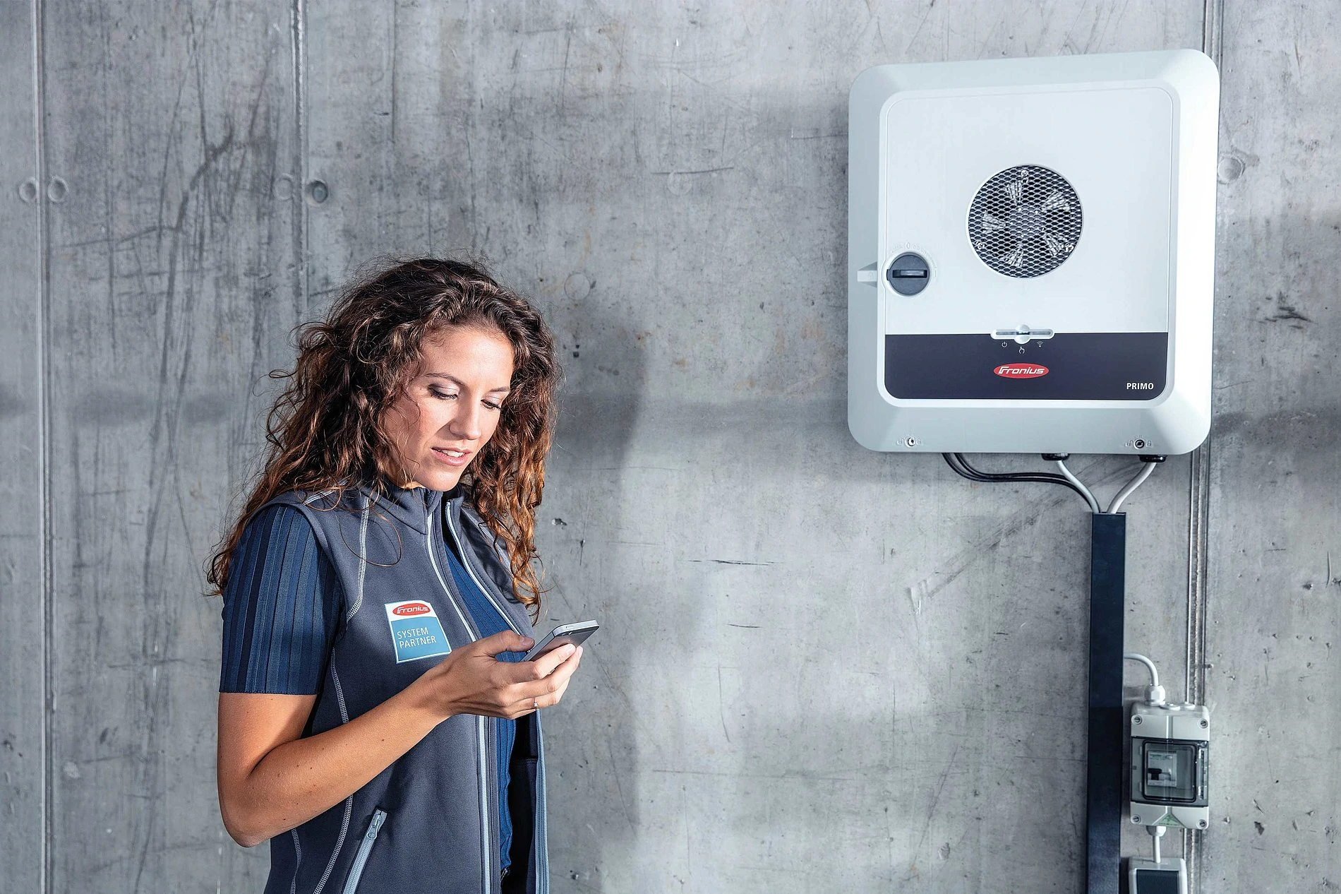 New Fronius Inverter (GEN24) on a concrete wall with a female technician checking the app