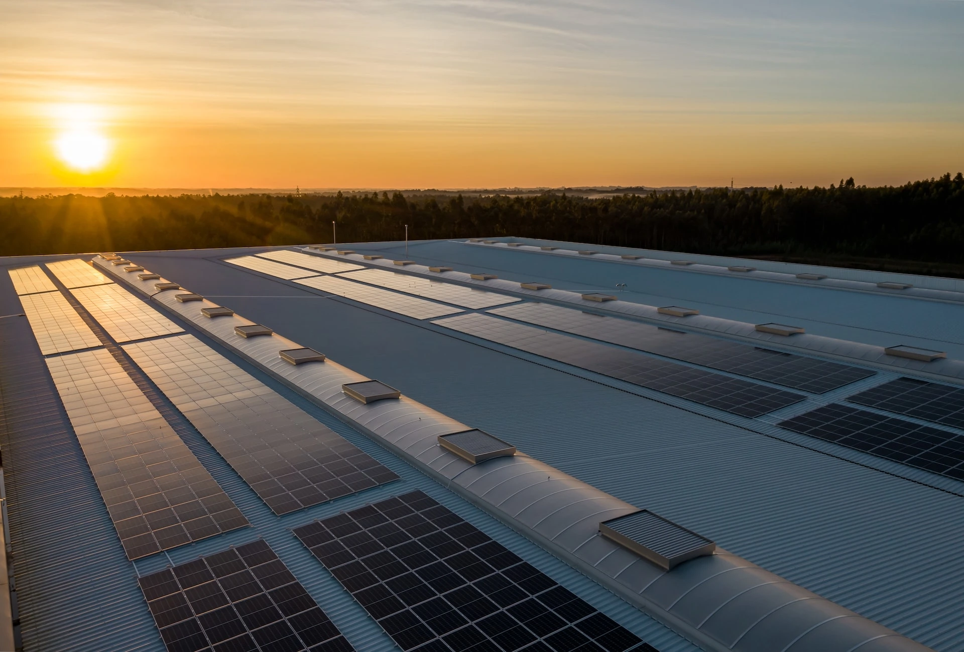Higher power solar panels installed on a factory roof with an orange sunset setting in the background