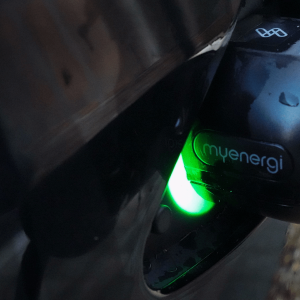 Close up of a myenergi zappi ev charger black socket plugged into a black car inlet with water droplets on the paintwork